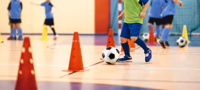 Child kicking soccer ball in between cones indoors