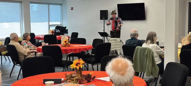 Active adults enjoying a social lunch program with live accordion music in a community setting.