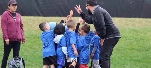 Children and coach putting their hands in the middle of a circle to do a team cheer