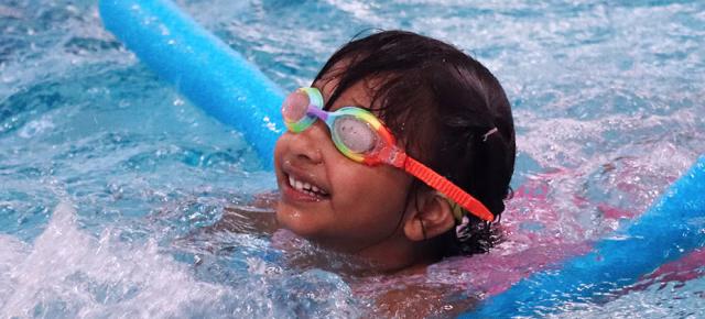 Girl with googles and a swim noodle at swim lessons